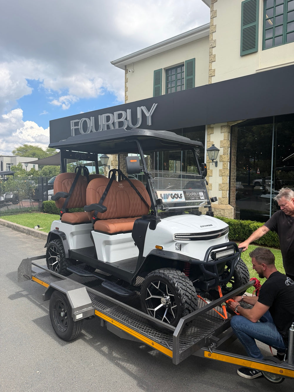A white golf cart being loaded onto a trailer outside Fourbuy