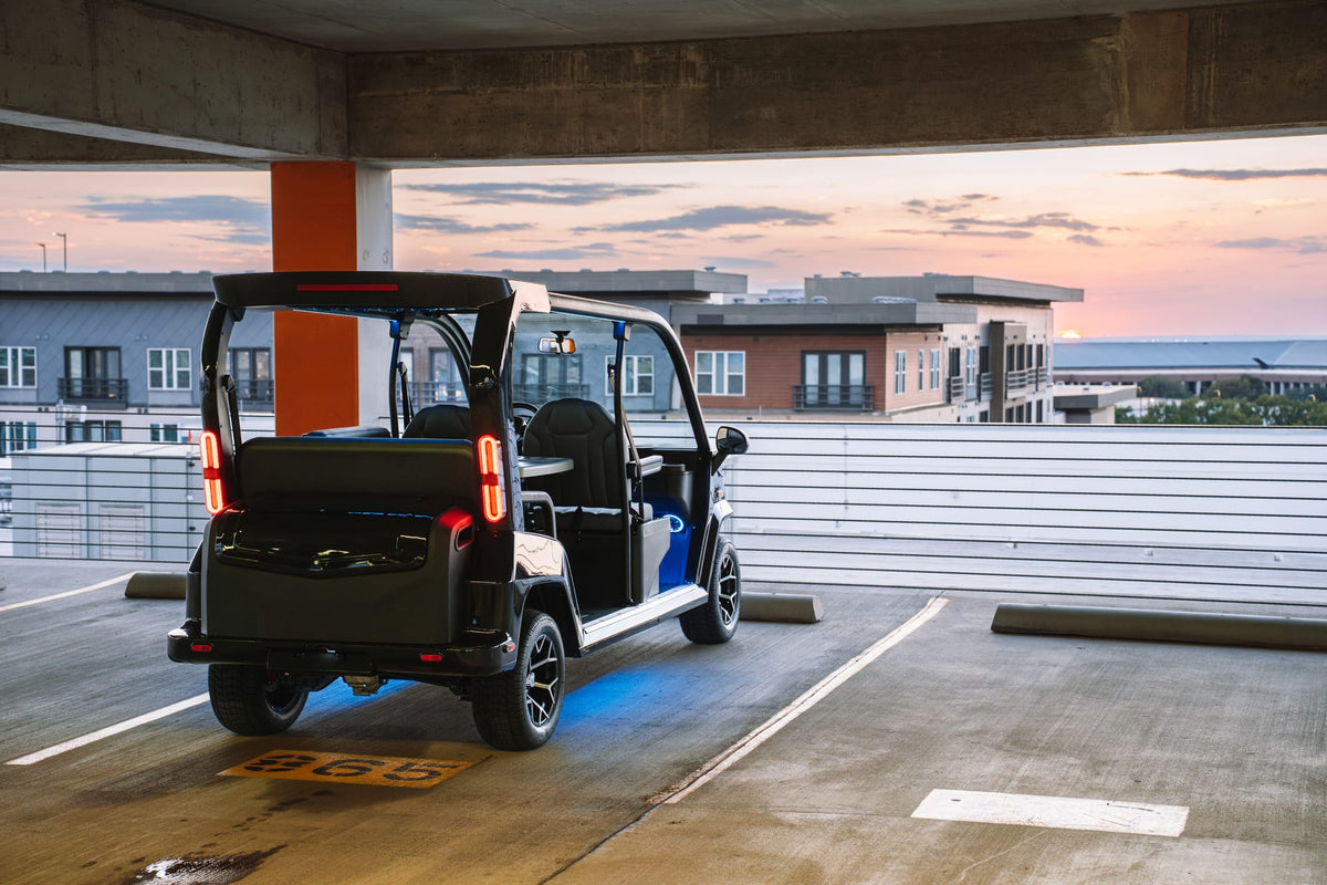 Rear view of a black Denago City with illuminated tail lights in a parking deck at sunset