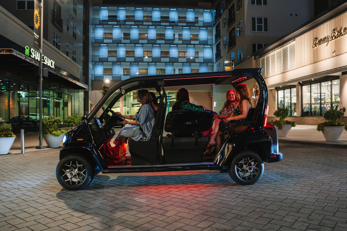 Friends seated in a black Denago City outside illuminated shops and restaurants at night