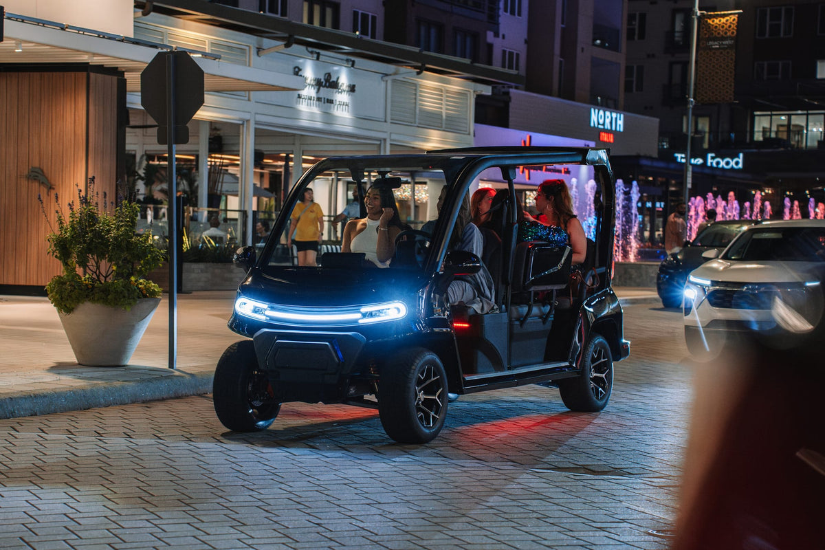 Denago City travelling past restaurants at night with its front LED lights illuminated