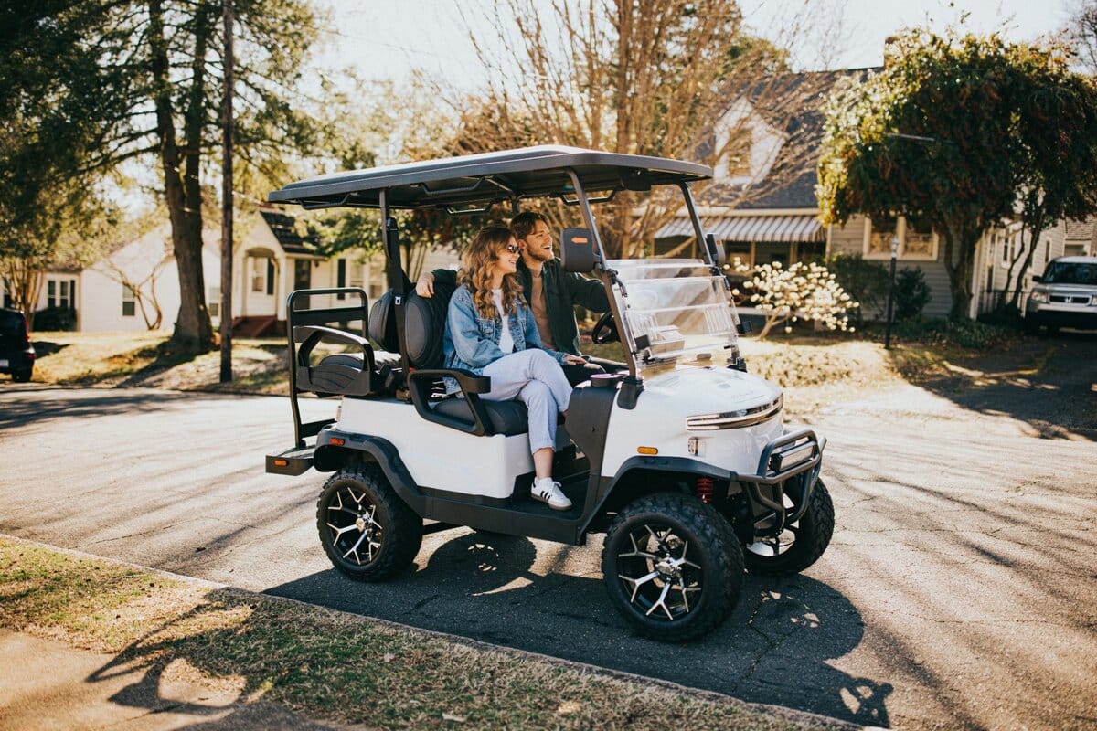 White Denago Nomad XL electric golf cart with a couple on a leafy residential street