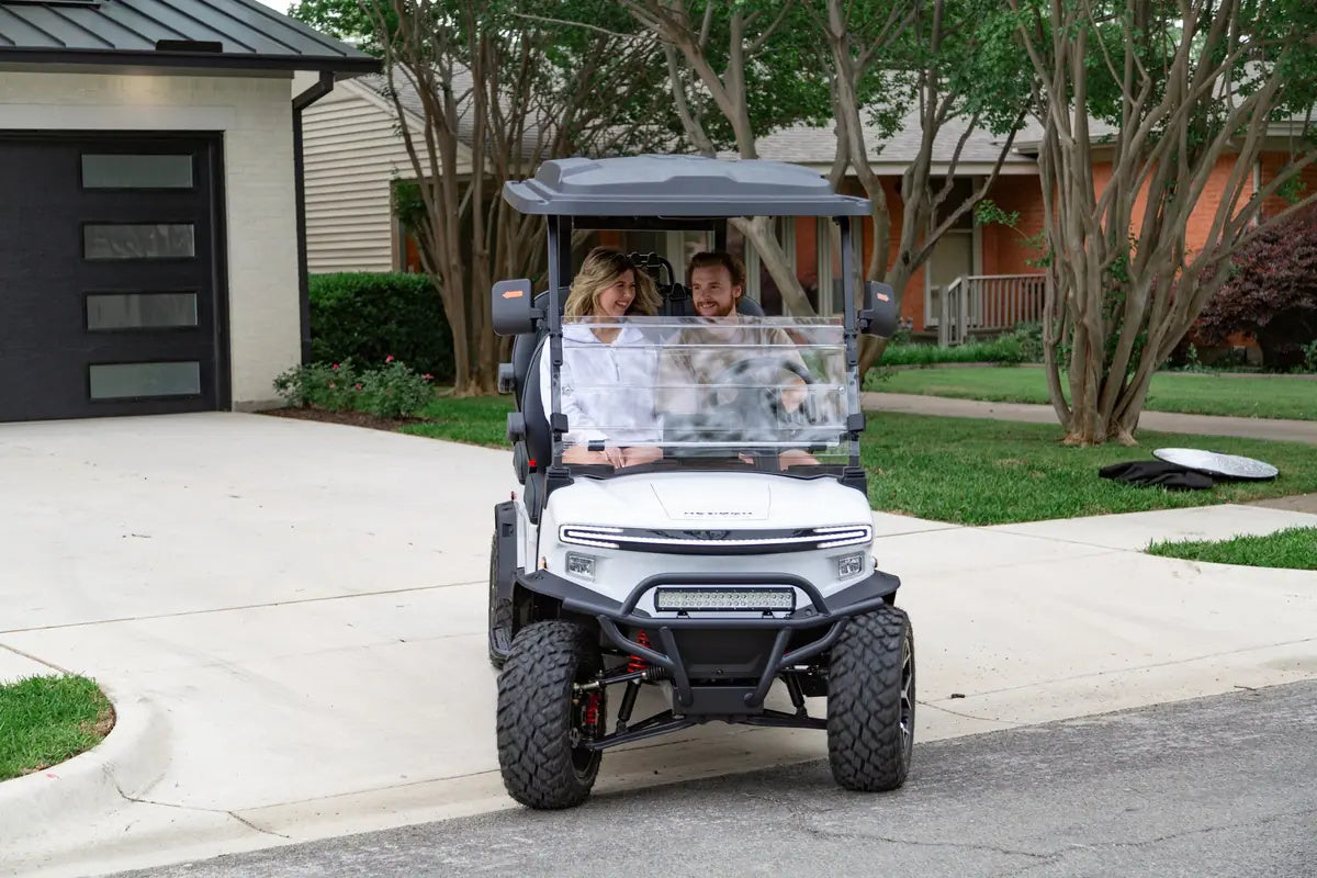 Couple in a white Denago Rover XL leaving a driveway outside their home
