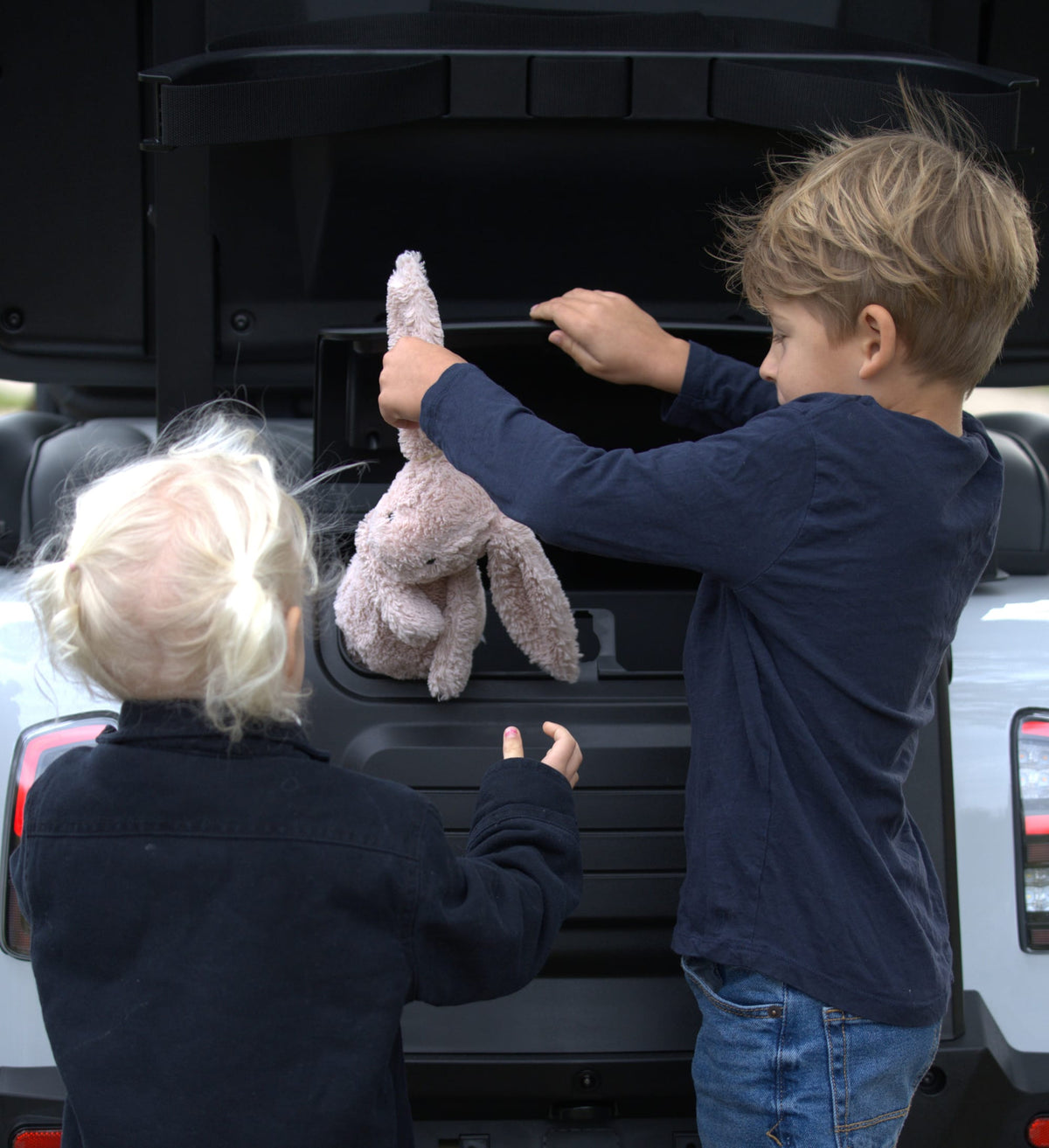 Children packing a soft toy into the rear storage compartment of a Denago Rover XXL