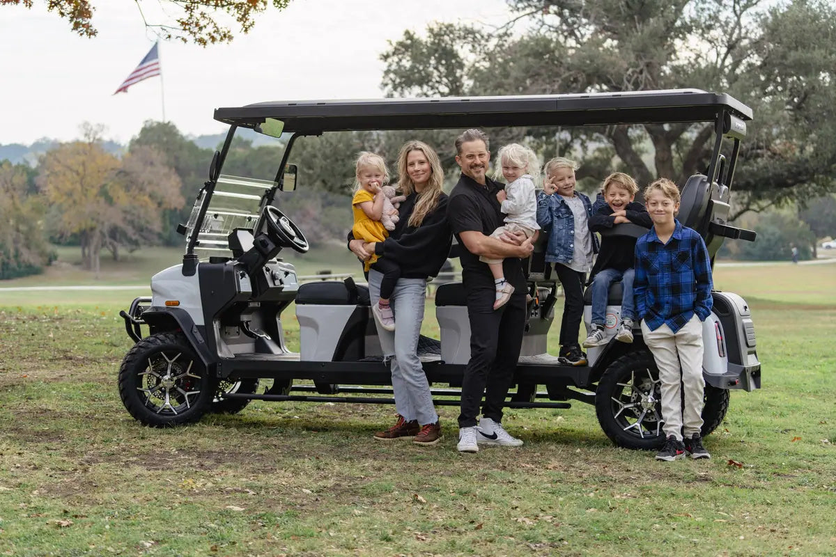 Family beside a white Denago Rover XXL with three forward-facing seating rows in a grassy park